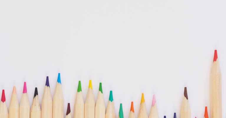 A row of vibrant colored pencils aligned on a white background, providing ample copyspace.